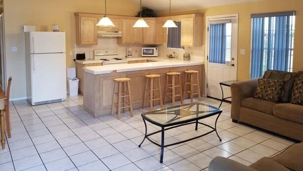A compact kitchen with a central island, wooden stools, and a glass-top table.