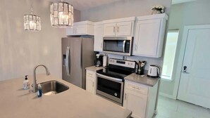 A modern kitchen with white cabinetry, stainless steel appliances, a double sink, and a chandelier. - Bungalow Tarvana #2 (Port Isabel)