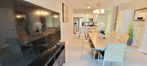A modern kitchen with a dining area, a large flat-screen TV, and a chandelier.