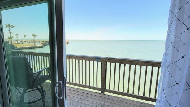 A balcony with a view of the ocean, a chair, and a wooden railing. - Bungalow Tarvana #2 (Port Isabel)