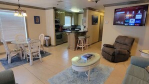 A living room with a dining area, kitchen, and a TV displaying streaming services. - Campeche Triplex Unit B (South Padre Island)