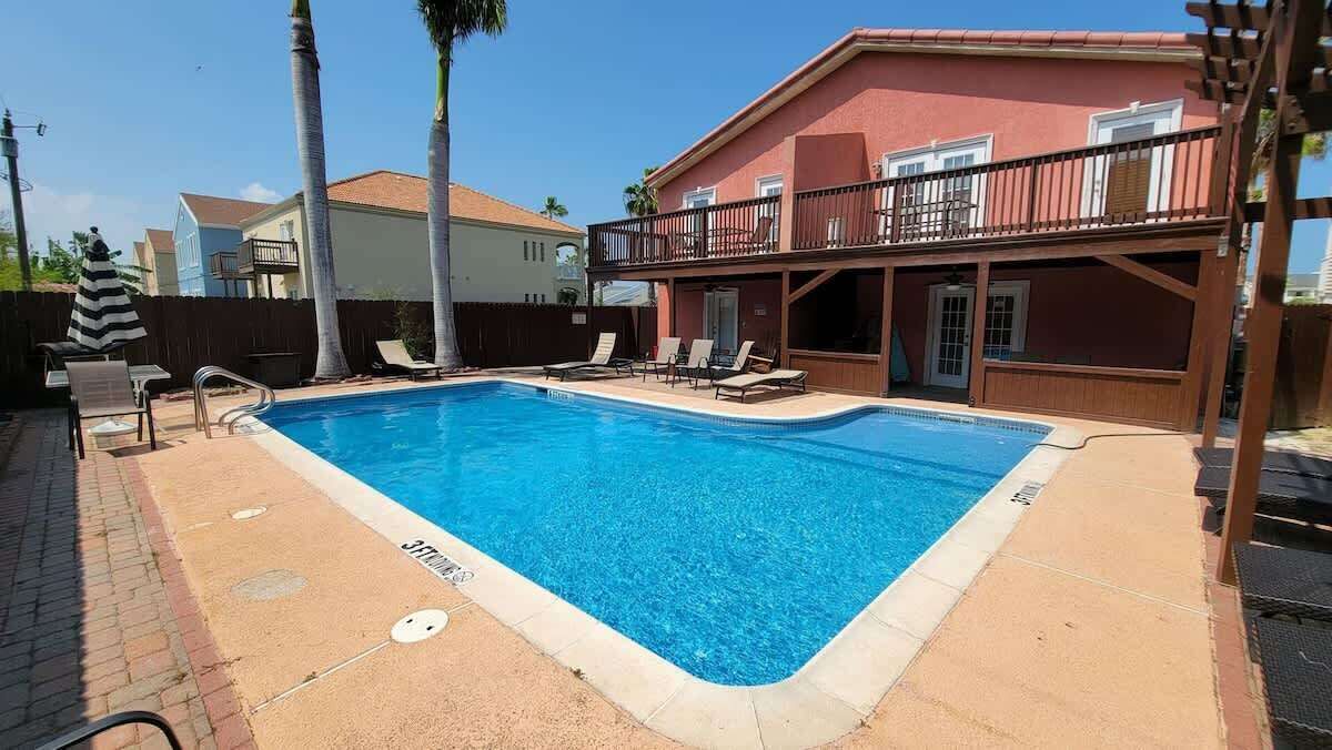 A rectangular swimming pool with a clear blue water surface, surrounded by a brick deck and lounge chairs.