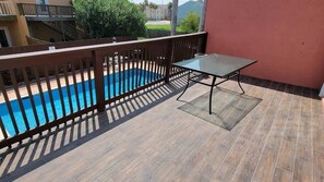 A balcony with a pool, a glass table, and a view of a residential area.