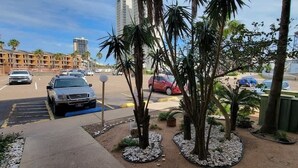 A parking lot with several cars, palm trees, and a building in the background. - BBQ Pits Private Beach Access Pool & Hot Tub (South Padre Island)