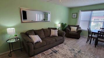 A living room with two couches, a dining table, chairs, a lamp, and a mirror on the wall.