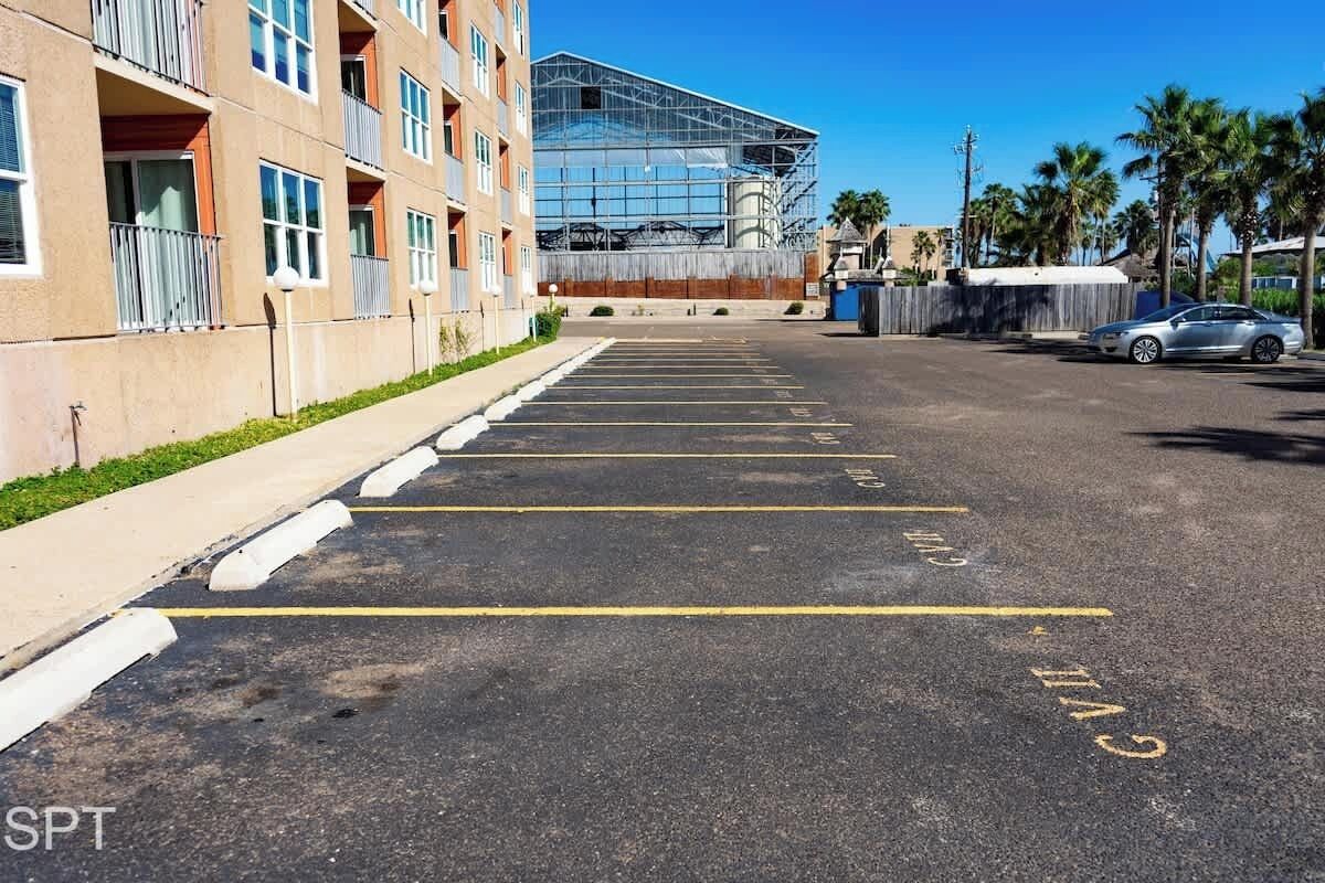 A parking lot with marked spaces and a building with multiple floors and balconies in the background.