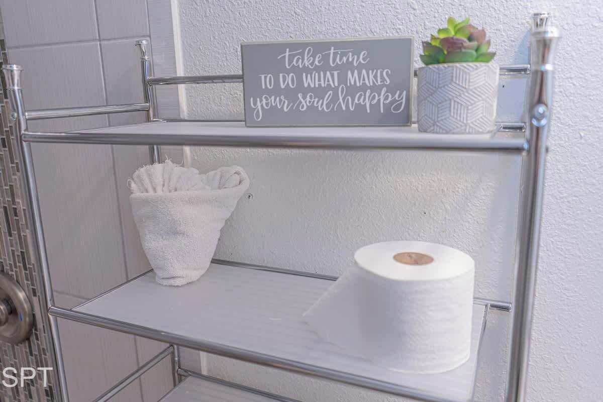 Une étagère en métal avec une pancarte, une petite plante en pot et un rouleau de papier toilette.