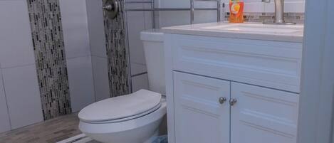 Un baño con inodoro, ducha con puerta de vidrio y lavamanos con dispensador de jabón.
