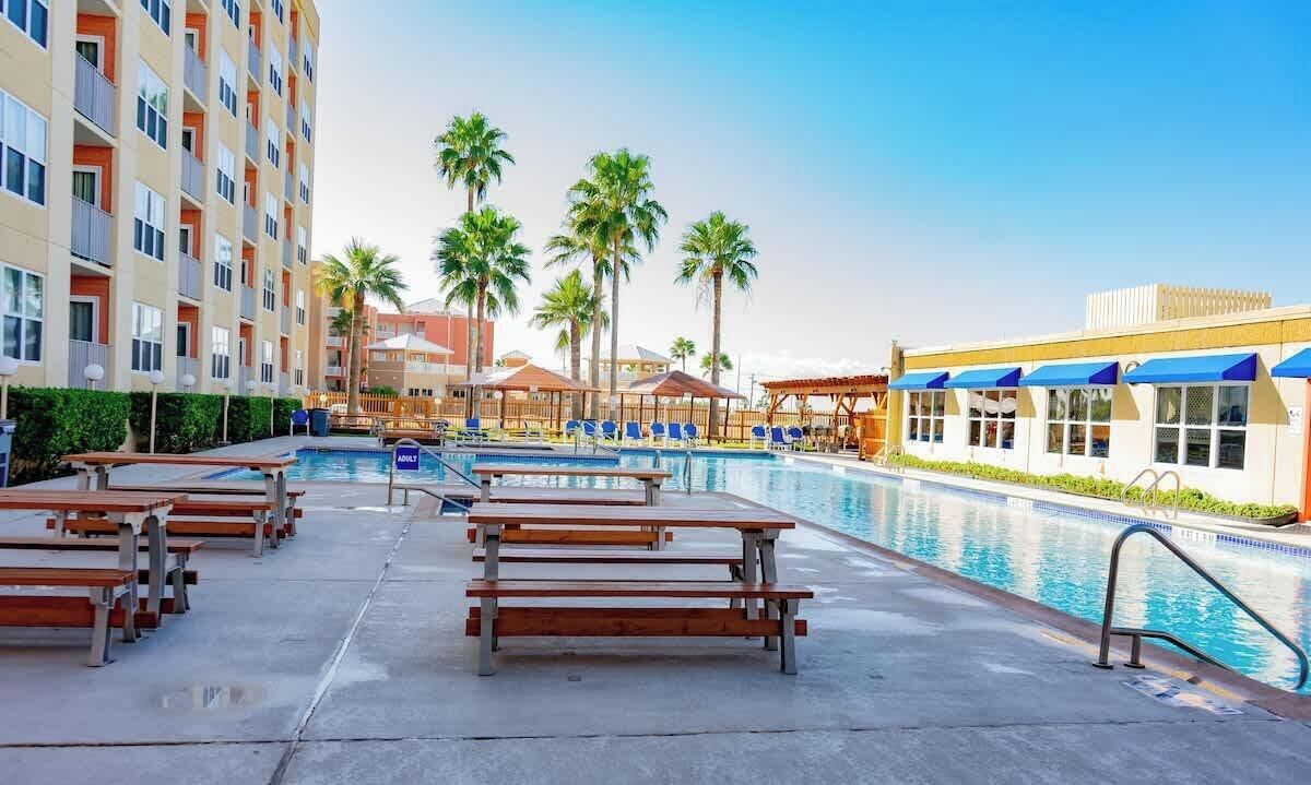 Un espace piscine d’hôtel comprenant plusieurs chaises longues, une piscine et des palmiers.