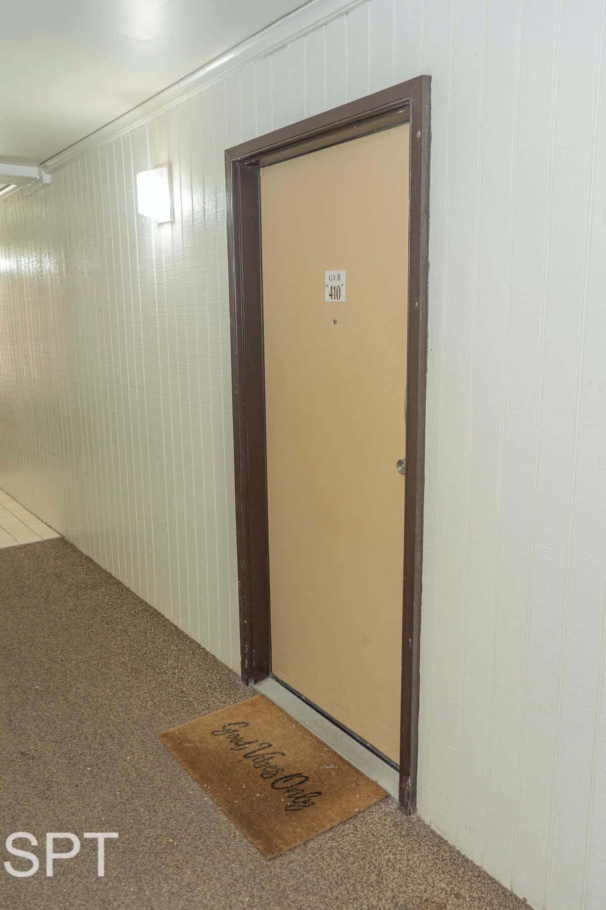 Um corredor com uma porta identificada com o número 410 e um tapete de entrada com uma mensagem.