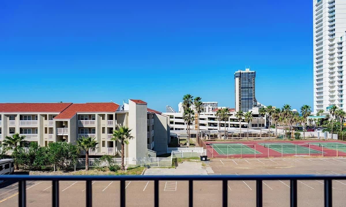 Un hotel de varios pisos con techo rojo, junto a un estacionamiento con canchas de tenis.