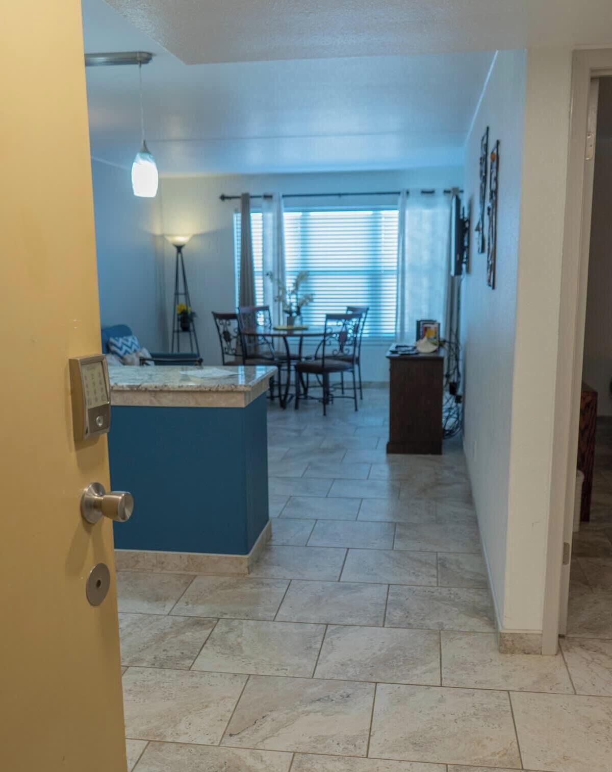 A kitchen with a blue island, dining table, chairs, and a window with blinds.