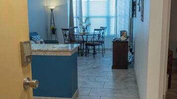 A kitchen with a blue island, dining table, chairs, and a window with blinds.