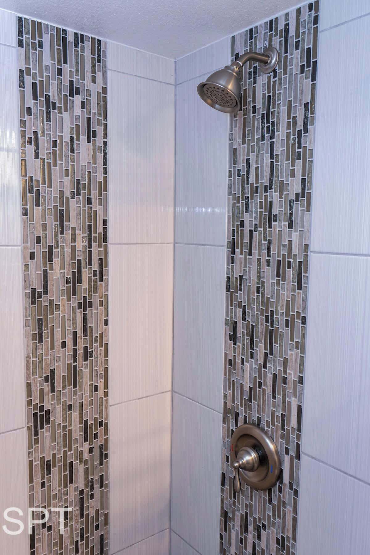 Eine Dusche mit Wand aus Mosaikfliesen und einer Handbrause.