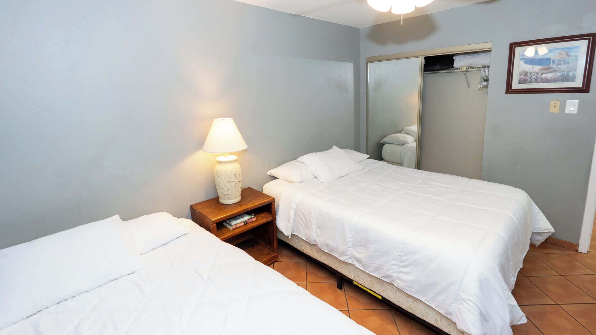 Ein Schlafzimmer mit zwei Betten, einem Nachttisch mit Lampe, einem Spiegel und einem gerahmten Bild an der Wand.