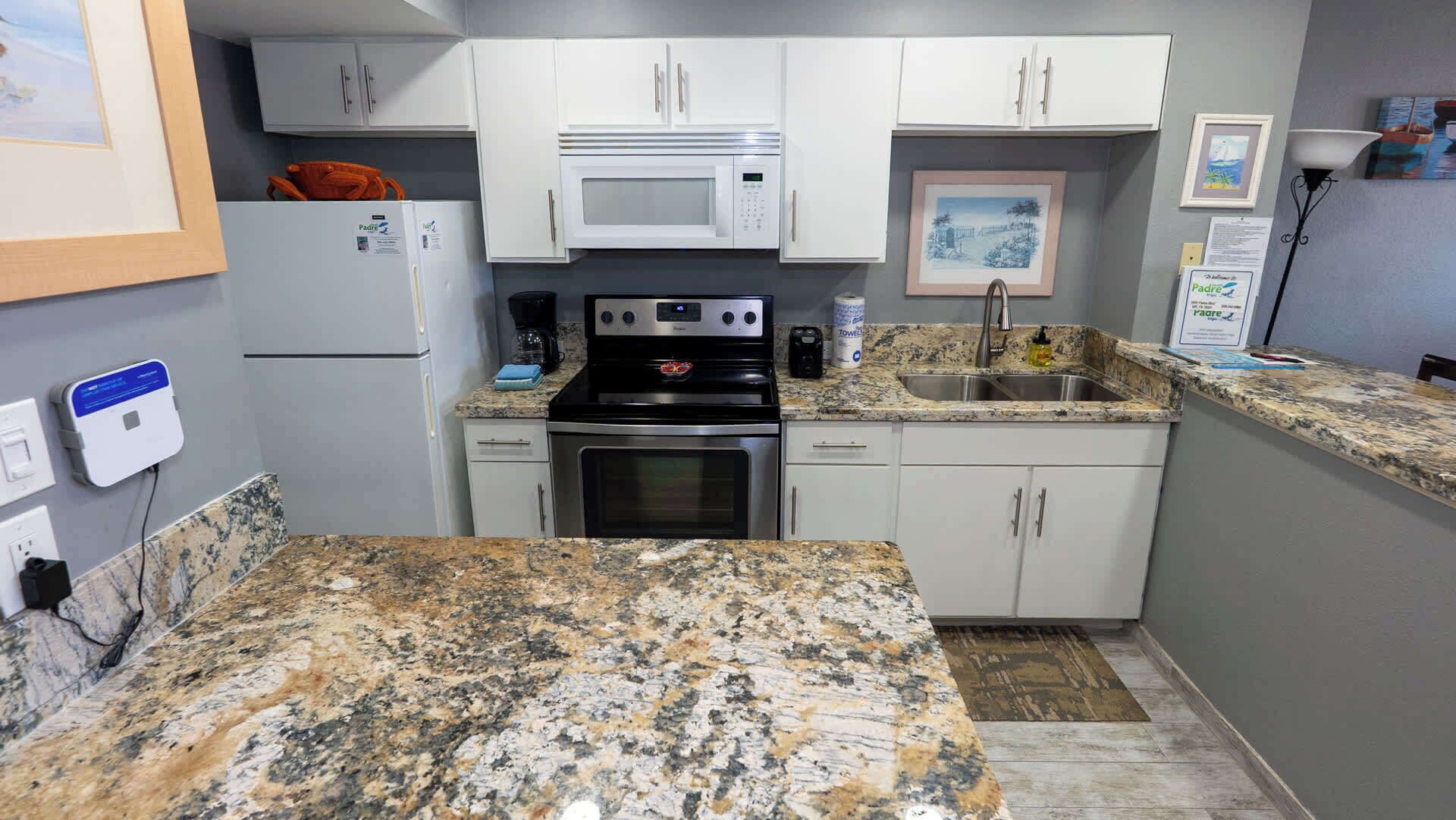 Una cocina compacta con armarios blancos, un microondas, una estufa y un lavabo.