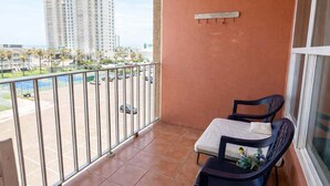 A balcony with a view of tall buildings, a metal railing, and a chair with a cushion.