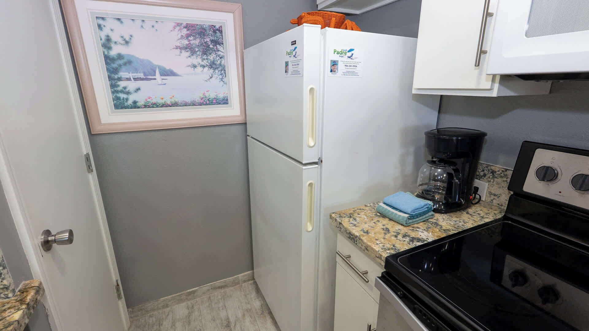 A compact kitchen with a refrigerator, a coffee maker, and a stove.