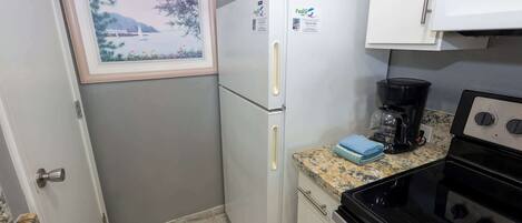 A compact kitchen with a refrigerator, a coffee maker, and a stove.