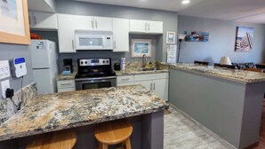 A kitchen with white cabinets, a granite countertop, a stove, and a microwave. There are two stools at the counter.