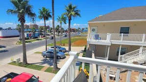 A residential area with a two-story building, palm trees, parked cars, and a clear sky.