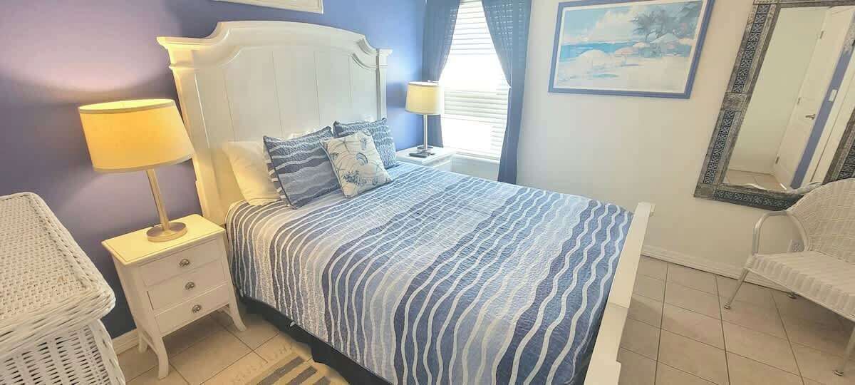 A bedroom with a bed, nightstands, a lamp, a chair, and a painting on the wall.