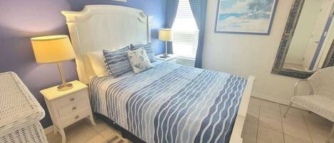 A bedroom with a bed, nightstands, a lamp, a chair, and a painting on the wall.