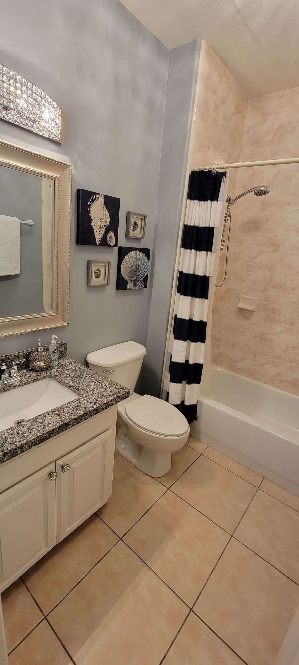 Ein Badezimmer mit Granitwaschtisch, Toilette, Badewanne mit Duschkopf und einer gestreiften Duschvorhang.