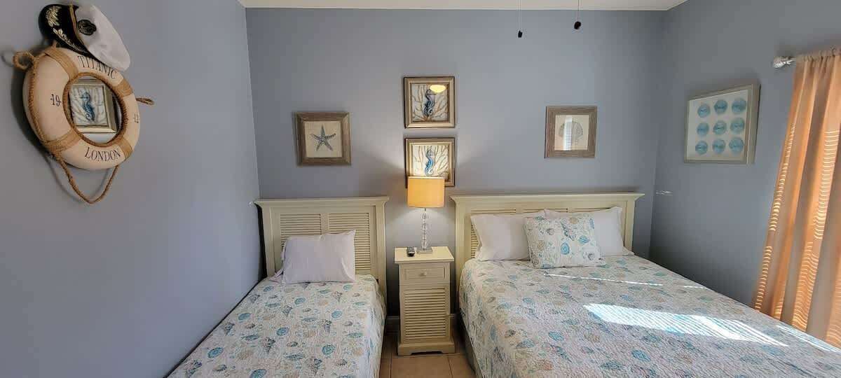 Un dormitorio con dos camas, una mesita de noche con lámpara y adornos en la pared, incluyendo cuadros y un círculo salvavidas.