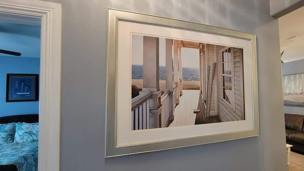 A framed coastal photograph on a wall, a brown leather sofa, and a white chair in a room with light-colored walls. - EZ Walk to Beach - Modern 2 Bedroom - Sleeps Many (South Padre Island)