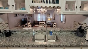A kitchen with granite countertops, a double sink, and white cabinets. There is a chandelier above the sink and a dining area in the background. - EZ Walk to Beach - Modern 2 Bedroom - Sleeps Many (South Padre Island)