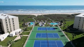 Un complesso con campi da tennis, edifici adiacenti, area piscina e vista sulla spiaggia.