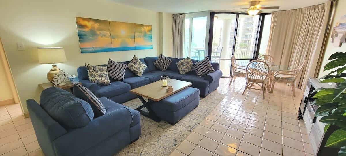 Una sala de estar con un sofá azul, una mesa de centro y una zona de comedor con sillas de mimbre.