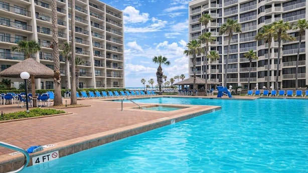 A hotel pool area with a 4 FT depth marker, lounge chairs, and palm trees. - Heated Pool - Sleeps Many Beachfront Resort (South Padre Island)