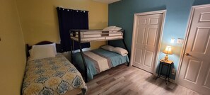 Cozy bedroom with a bunk bed and single bed, featuring a traditional door and a small table with a lamp.