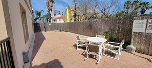 Relax in this patio area with a round table and four chairs, surrounded by lush greenery and a wooden fence.
