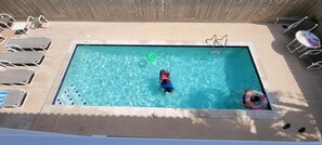 Relax by the pool with lounge chairs and a table, surrounded by a tiled deck and a lifeguard stand for added safety.