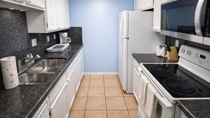 Une cuisine compacte avec des meubles blancs, un évier en acier inoxydable, un four encastré, un four à micro-ondes et une plaque de cuisson.