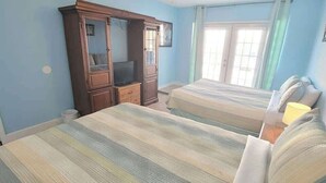 Une chambre avec deux lits, une armoire, un téléviseur et une fenêtre avec des rideaux.