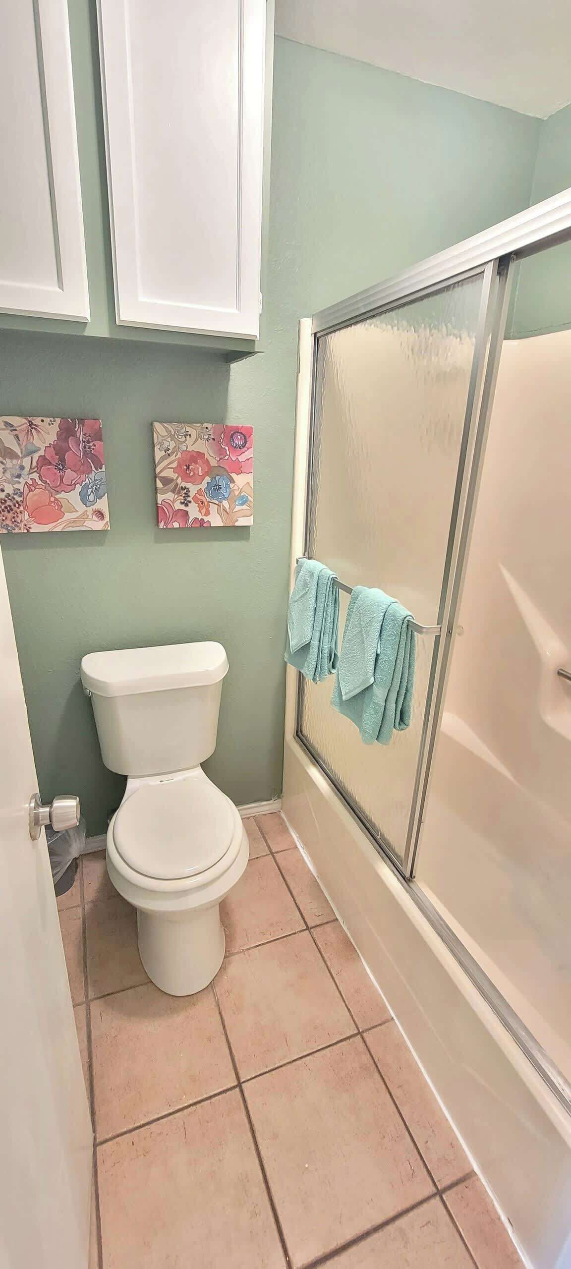 Ein Badezimmer mit Toilette, Dusche und zwei Blumenbildern an der Wand.