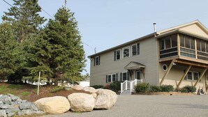 A two-story house with a front porch, large rocks, and a pine tree. - Modern Condo #2! (Ellsworth)