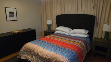 A neatly made bed with a patterned bedspread, two bedside tables with lamps, a framed picture on the wall, and a ceiling fan.