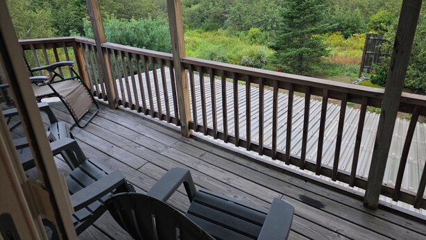 A wooden deck with a view of a grassy field and trees. - Modern Condo #2! (Ellsworth)
