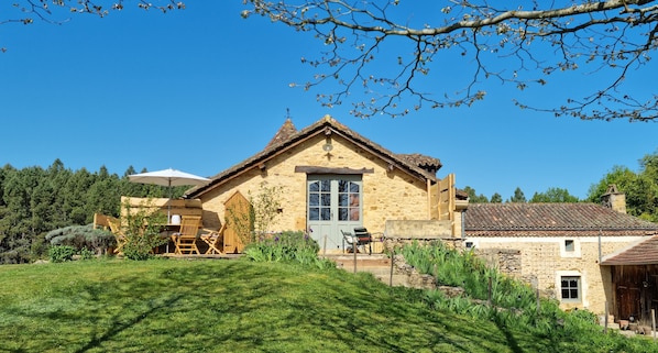 A stone house with a sloped roof, a wooden deck, and a garden.