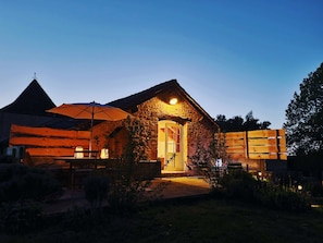 A stone building with a warm-lit entrance and a large umbrella.