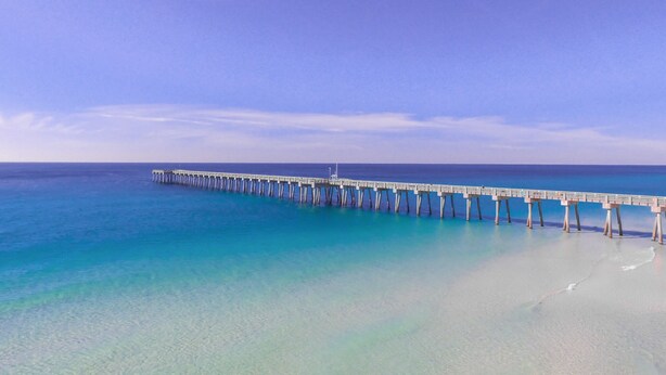 Eine lange Pier, die sich ins Meer erstreckt, mit klarem Wasser und blauem Himmel.