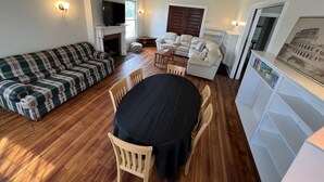 Ein Wohnzimmer mit Kamin, einer Couch, einem Esstisch und einem an der Wand befestigten Fernseher.