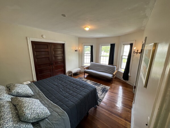 A bedroom with a large bed, a bench, and a sofa. There are two doors, one of which is a sliding door.