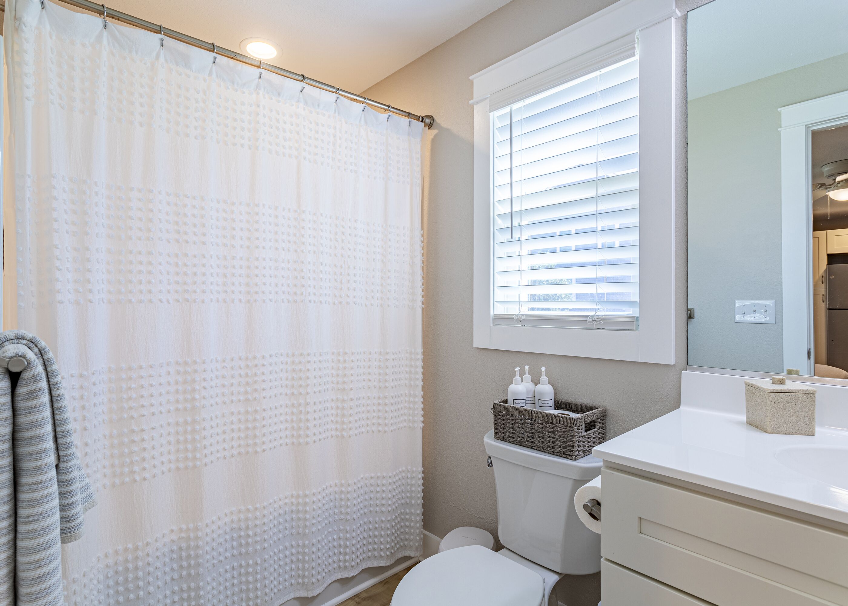 A bathroom with a shower curtain, toilet, and a window with blinds.