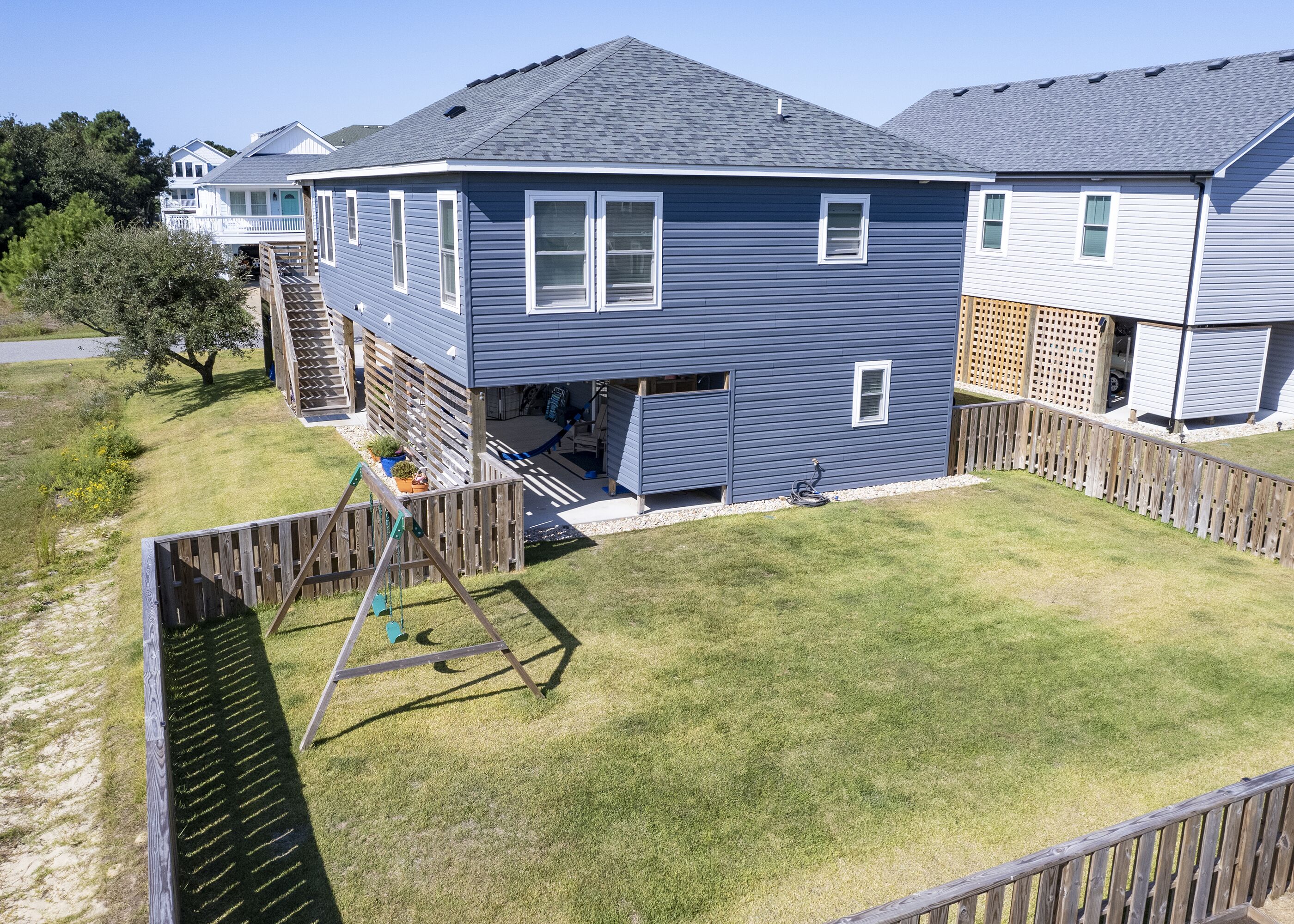 A two-story residential building with a fenced backyard, a swing set, and a small deck.